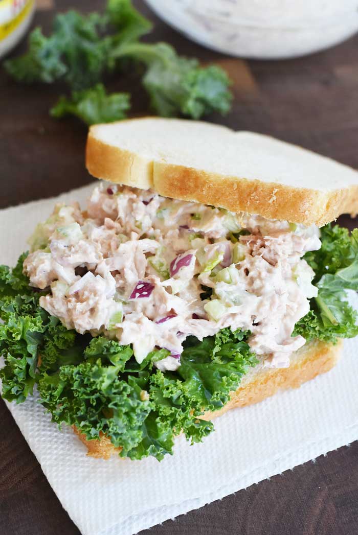 DChunky tuna on white bread with kale. This sandwich is on a wood platter with a white napkin.