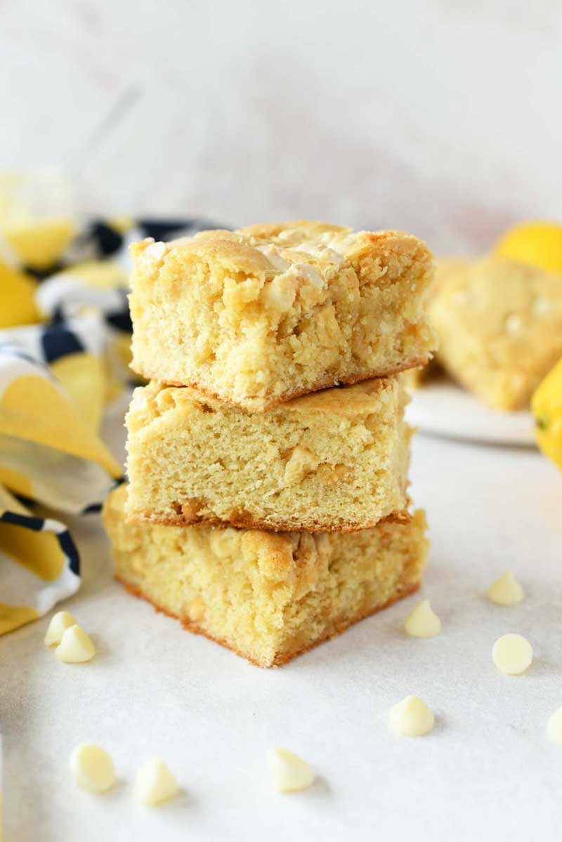 A stack of 3 fluffy lemon brownies on a white table with scattered white chocolate morsels.